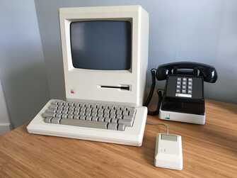 macintosh with keyboard and mouse next to modem with telephone on top of it, on a desk